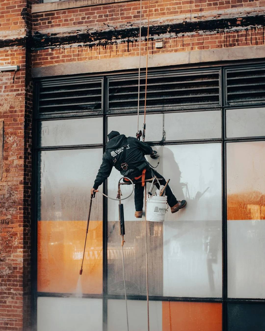 Two workers clean windows on a modern glass building facade using a suspended platform.